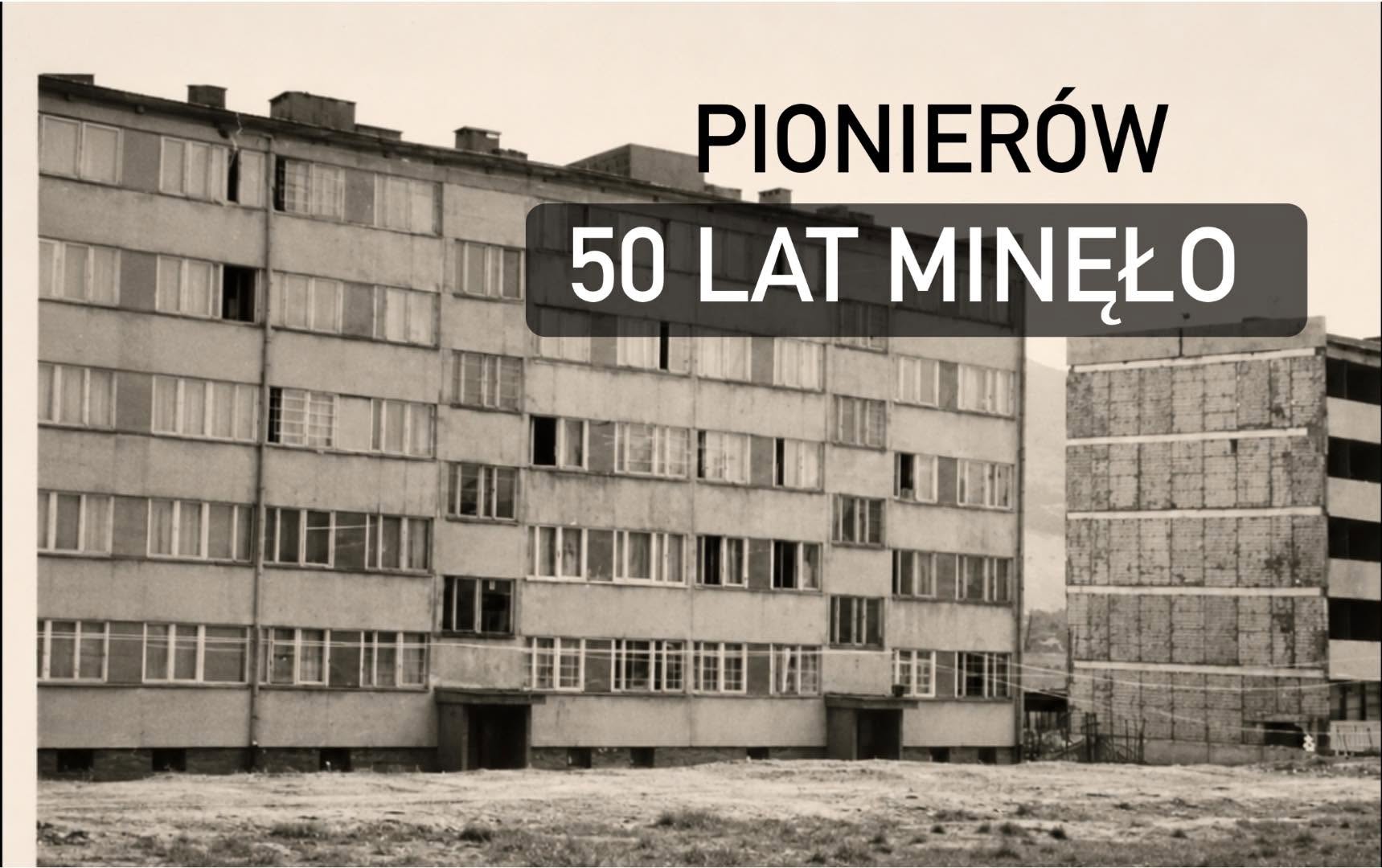 Czarno-biała fotografia przedstawiająca pierwszy budynek wielorodzinny przy ul. Pionierów w Głuszycy krótko po jego wybudowaniu. Widoczny jest pięciokondygnacyjny blok mieszkalny z licznymi oknami oraz fragment sąsiedniego budynku. Na zdjęciu umieszczono napis „Pionierów – 50 lat minęło”.