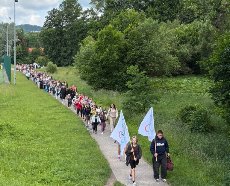 Pochód uczestników Głuszyckich Igrzysk Sportowych zmierza na stadion za flagami olimpijskimi.